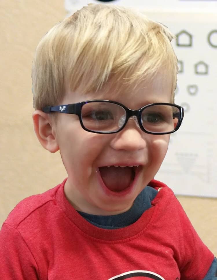 blonde boy in red shirt wearing black tomato glasses and grinning widely